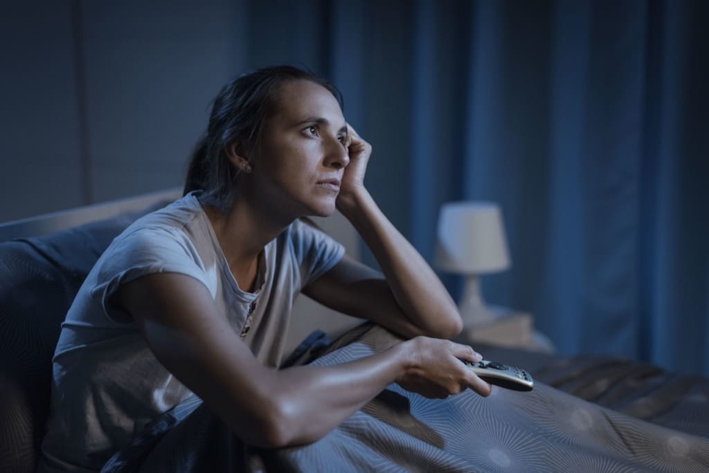 Frau liegt im Bett und schaut fern