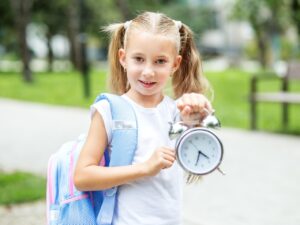 Ein kleiner fröhlicher Schüler mit einer Uhr