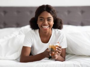 Fröhliche Afroamerikanerin genießt Kräutertee im Bett