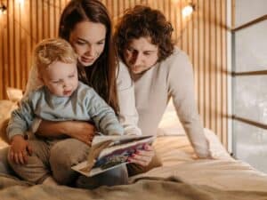 Ein Mann und eine Frau lesen ihrem Kind eine Geschichte vor - sie sitzen dabei auf einem Bett und es sieht gemütlich aus