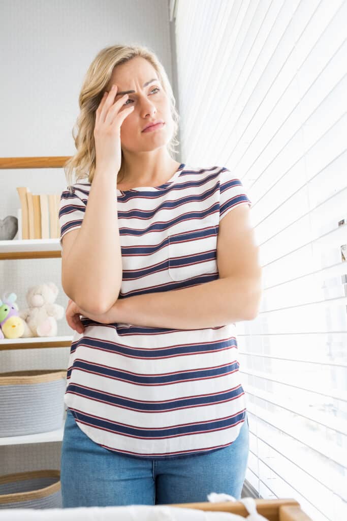 Eine Frau leidet unter Schlafmangel. Sie steht vor einem Fenster und hält sich die Hand an ihr beunruhigtes Gesicht