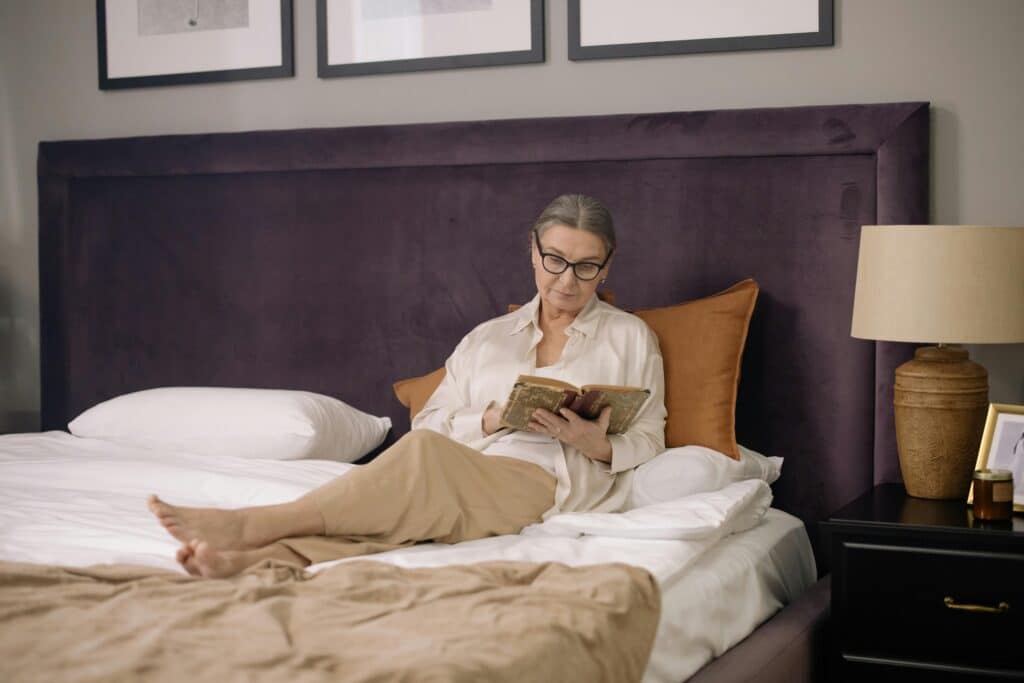 Ältere Frau liegt auf einem Boxspringbett und liest ein Buch